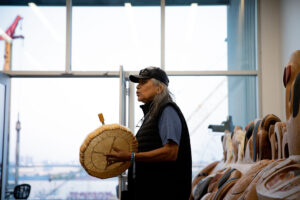 Xwalacktun, a Squamish Nation artist, drums in front of a totem pole.